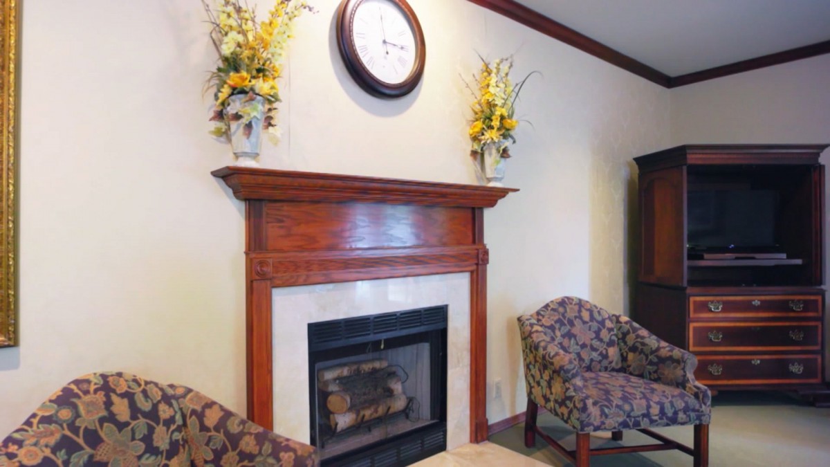 A cozy seating area featuring a wooden mantel adorned with floral arrangements and a clock above the fireplace.