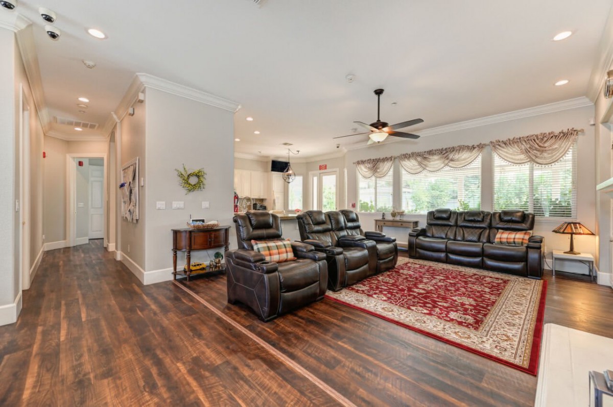 A spacious living room with recliner seating, a ceiling fan, and large windows offering plenty of natural light.