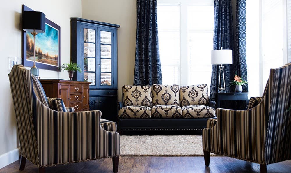 A stylish living room with patterned upholstery, featuring a sofa and armchairs, complemented by a cabinet and elegant curtains.