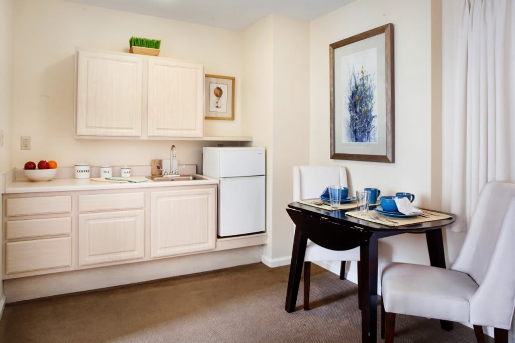 A cozy kitchen and dining area featuring a small table set for two, with white cabinets and a refrigerator nearby.