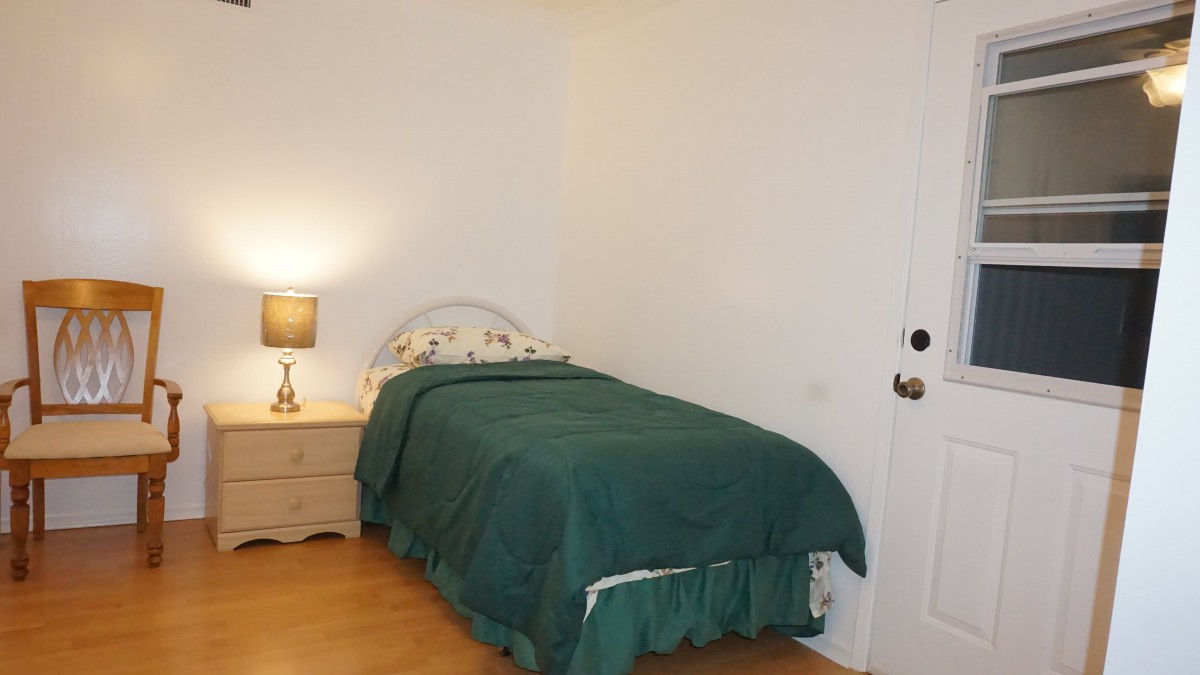 A minimalist bedroom with a single bed and a nightstand featuring a lamp.