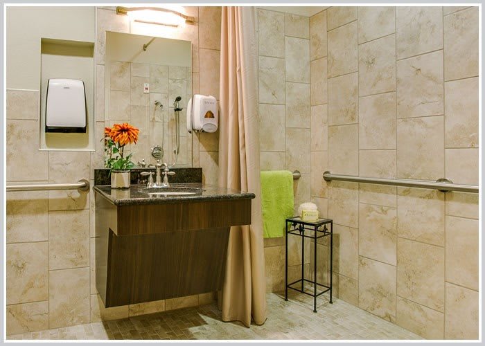 A modern bathroom with a sink, mirror, flower arrangement, and towel on a tiled wall.