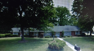 A suburban house with a large lawn and trees in the front yard.