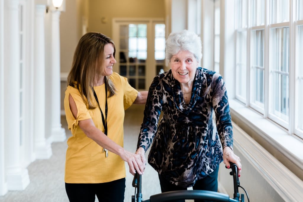 A caregiver assisting an elderly woman using a walker in a nursing home.