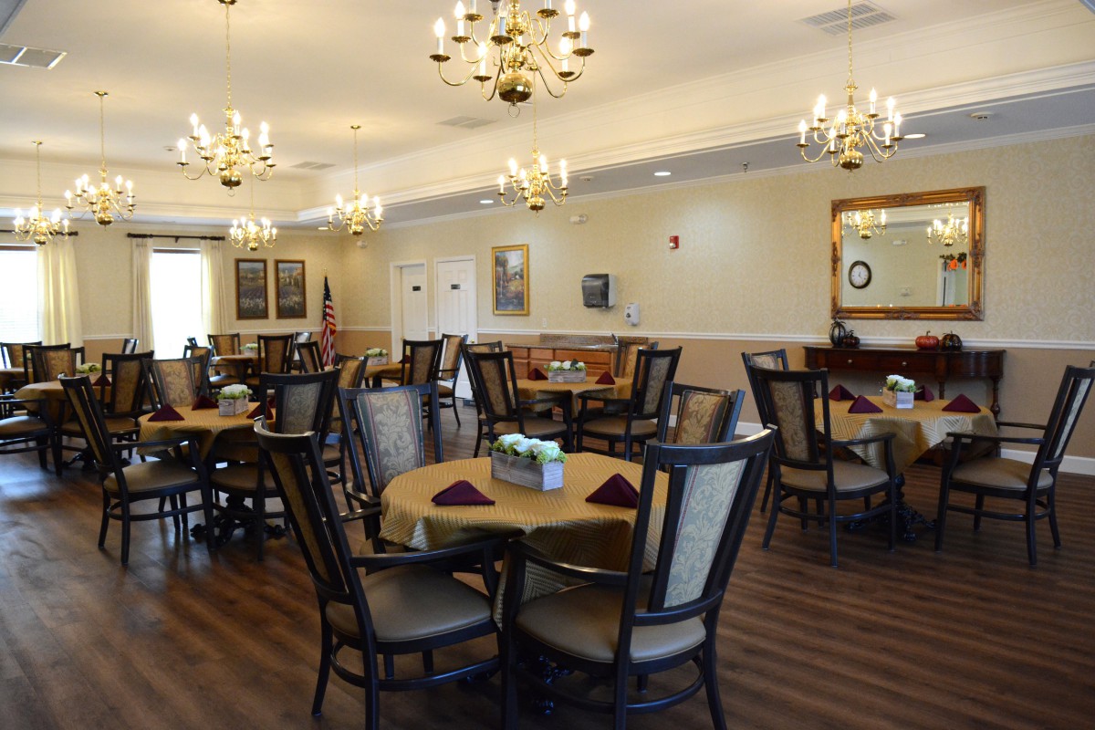 An elegant dining room with neatly arranged tables and chairs, illuminated by chandeliers.