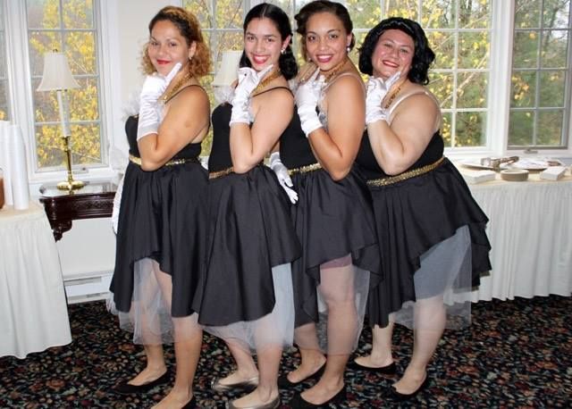 A group of women dressed in black dresses and white gloves, posing and smiling.