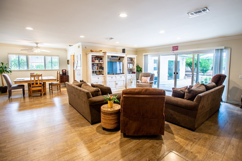 A cozy living room with comfortable sofas arranged around a center table, featuring a television and bookshelf in the background.