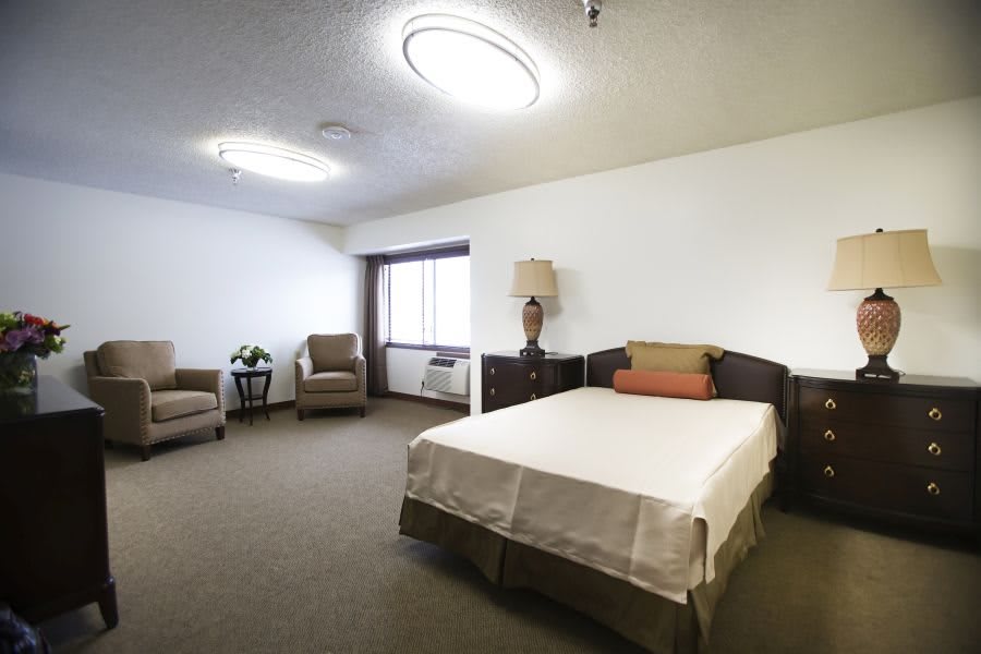 A minimalist bedroom with a bed, chairs, and a lamp.