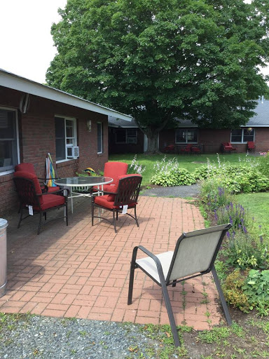 A cozy outdoor patio area with red chairs and a table, surrounded by greenery.
