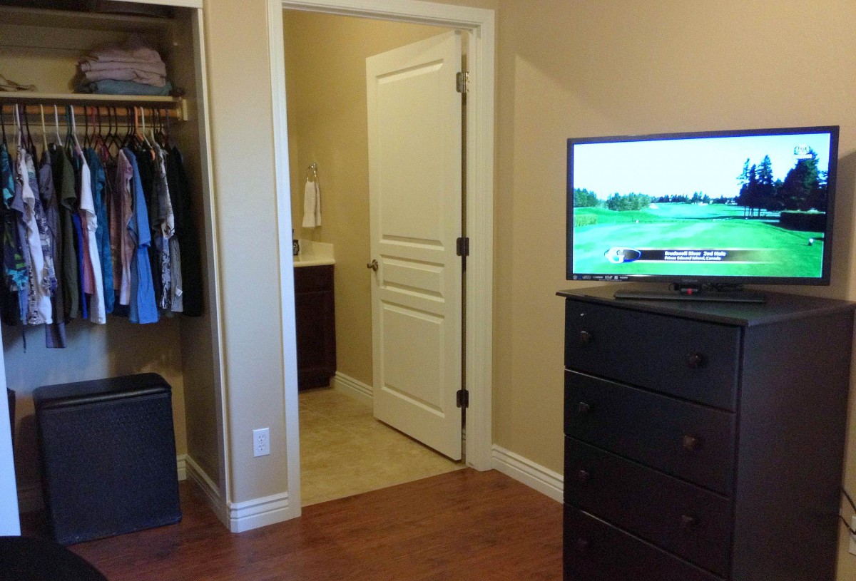 A bedroom with an open closet, a dresser topped with a television, and a view into an adjoining bathroom.