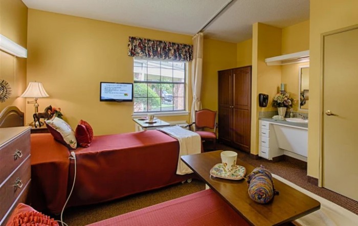 A cozy bedroom with twin beds, a TV mounted on the wall, and a small sitting area by the window.
