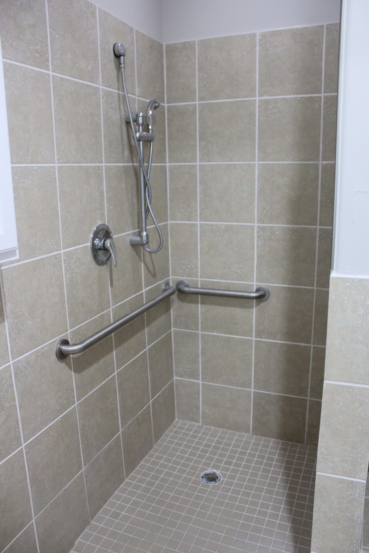 A tiled accessible shower with handrails and a showerhead.