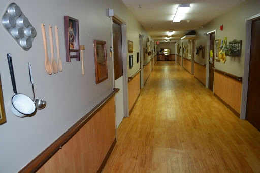 A well-lit hallway featuring wooden flooring, decorated walls, and several doors leading to individual rooms.