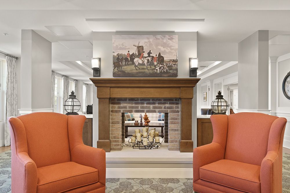 A cozy living room featuring a central fireplace, framed by orange chairs and adorned with artwork above the mantel.