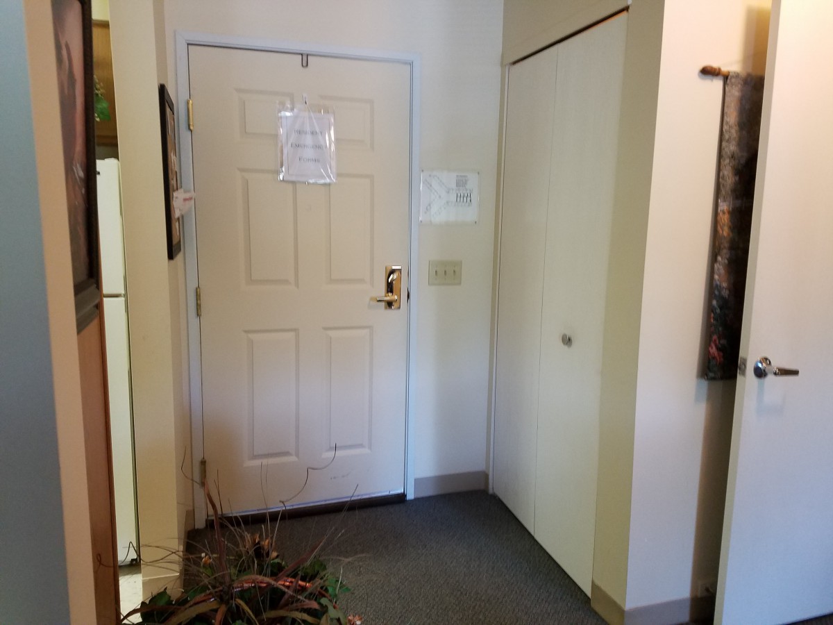 An interior view of an apartment entrance with a door, hallway, and notice posted on the door.