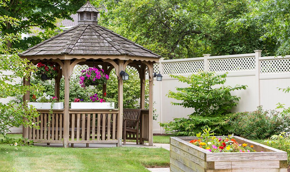 A picturesque garden with a wooden gazebo surrounded by vibrant flowers and greenery.