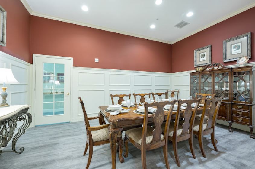 A stylish dining room with a large wooden table and chairs, set against red walls with white wainscoting.