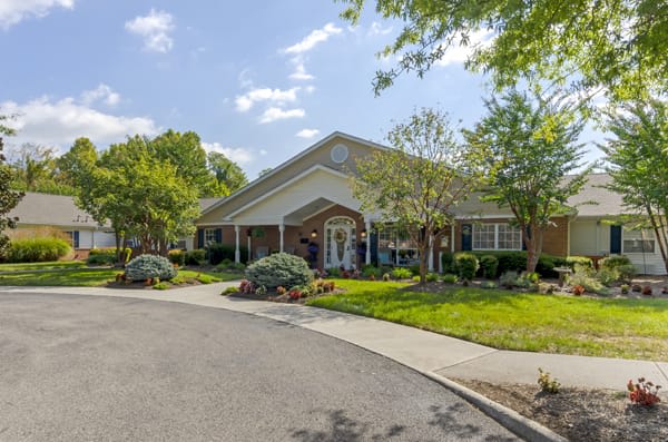 A charming single-story building surrounded by lush greenery and a well-maintained driveway under a clear blue sky.
