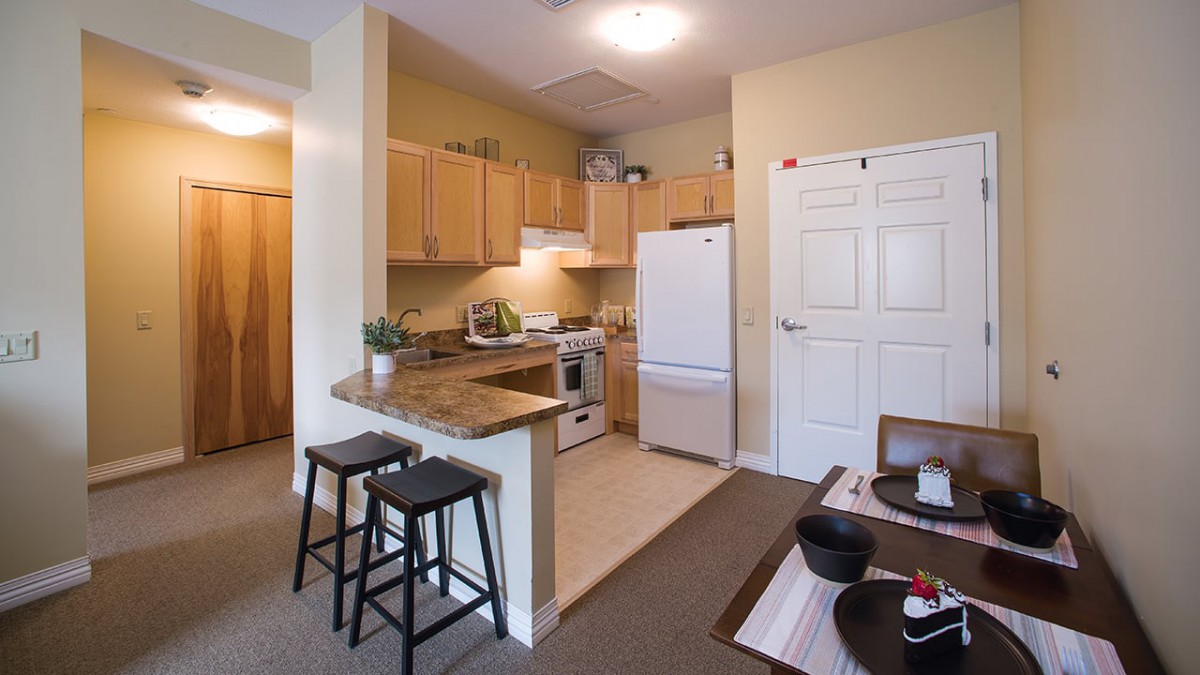 A cozy apartment kitchen with wooden cabinets, a white refrigerator, and seating at the countertop.