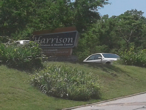 A view of the Harrison sign with a car parked nearby amidst greenery.