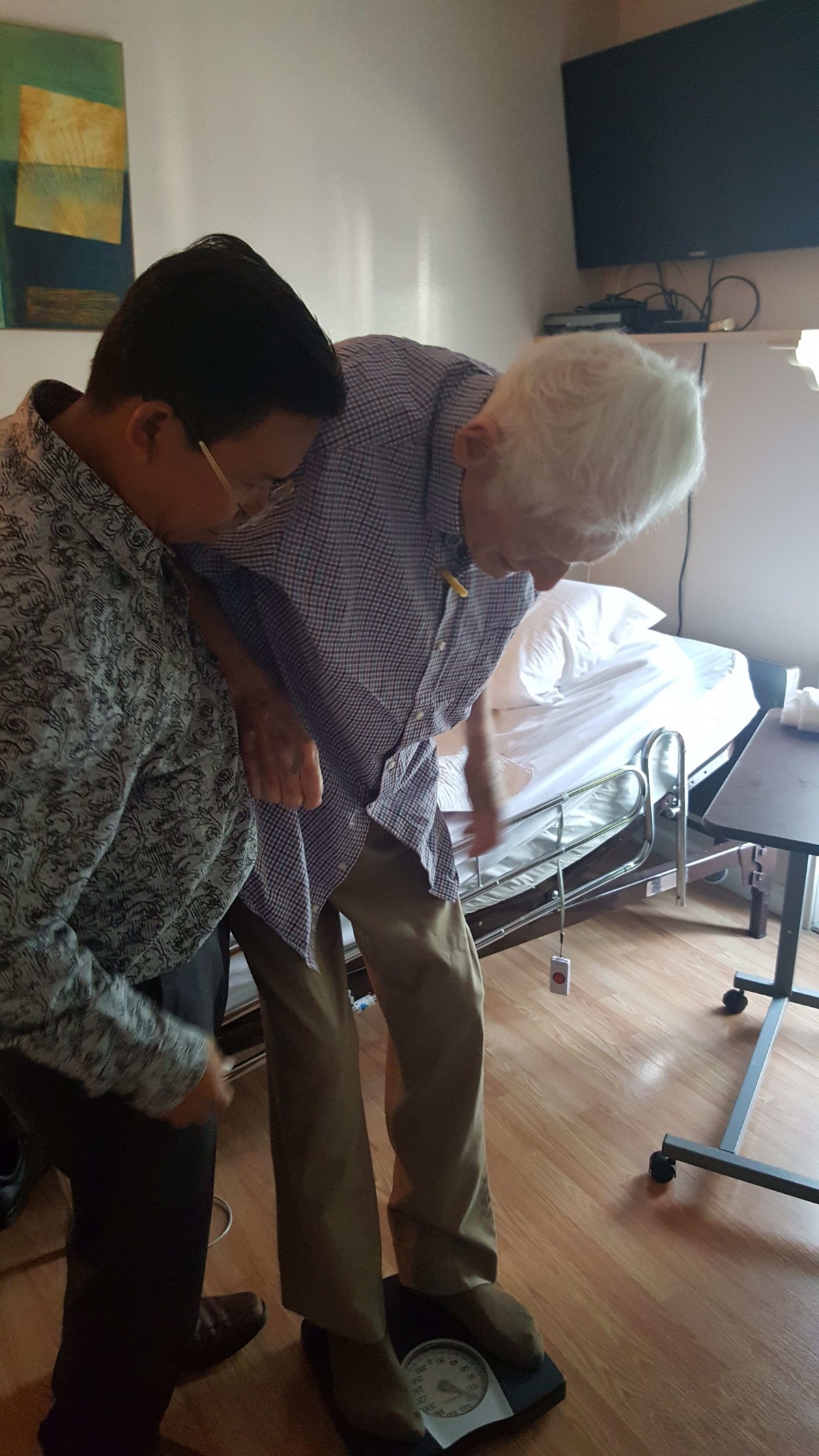 A caregiver assists an elderly person in a hospital room.