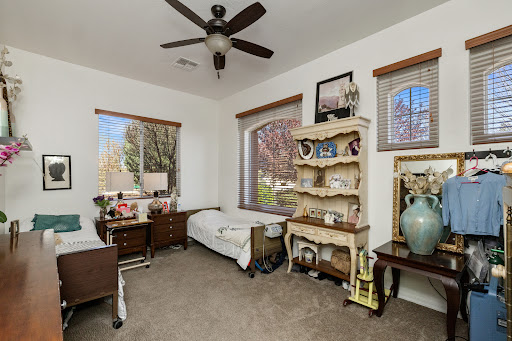 A cozy and well-decorated bedroom featuring a ceiling fan, natural light from large windows, and stylish furniture.