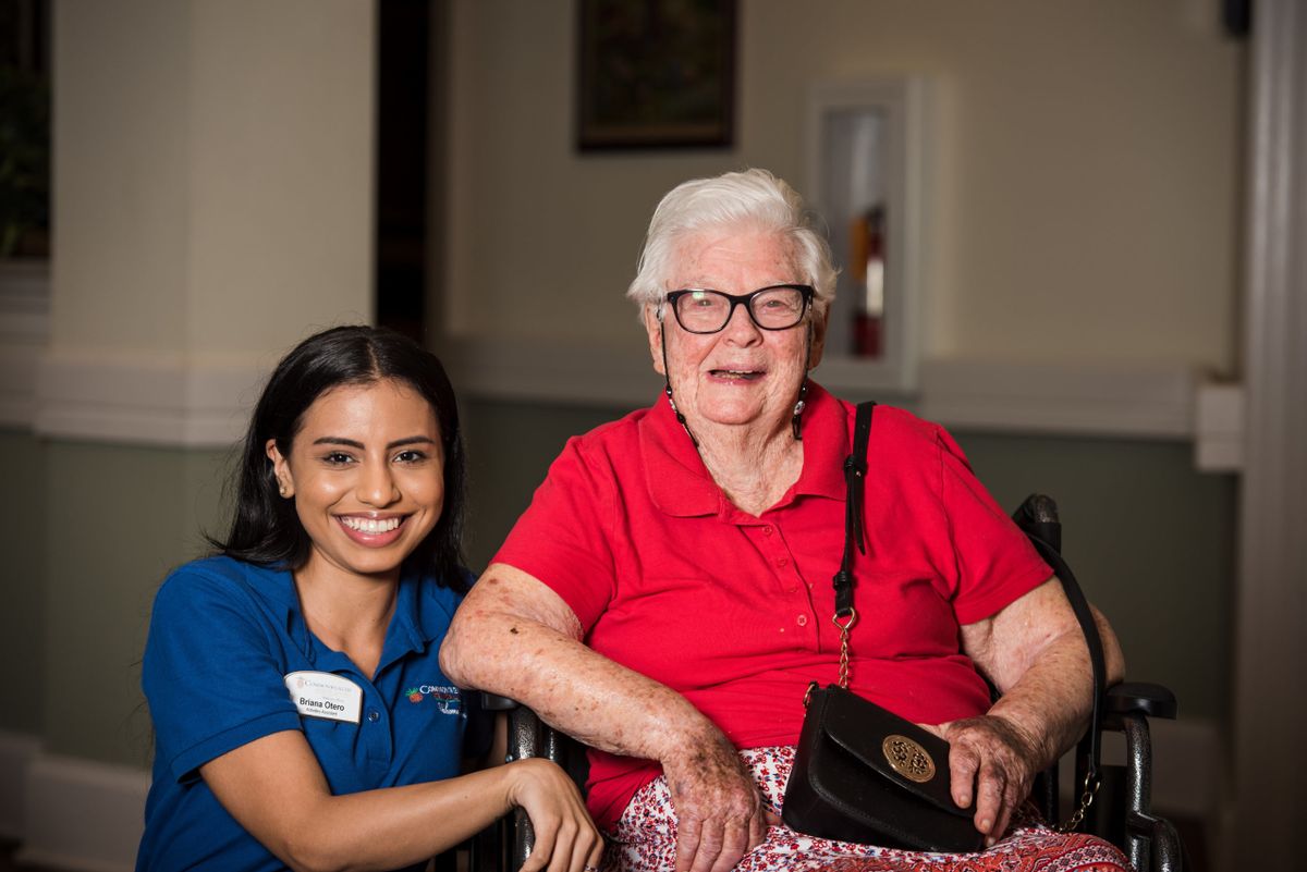 A caregiver smiling with an elderly woman in a wheelchair.
