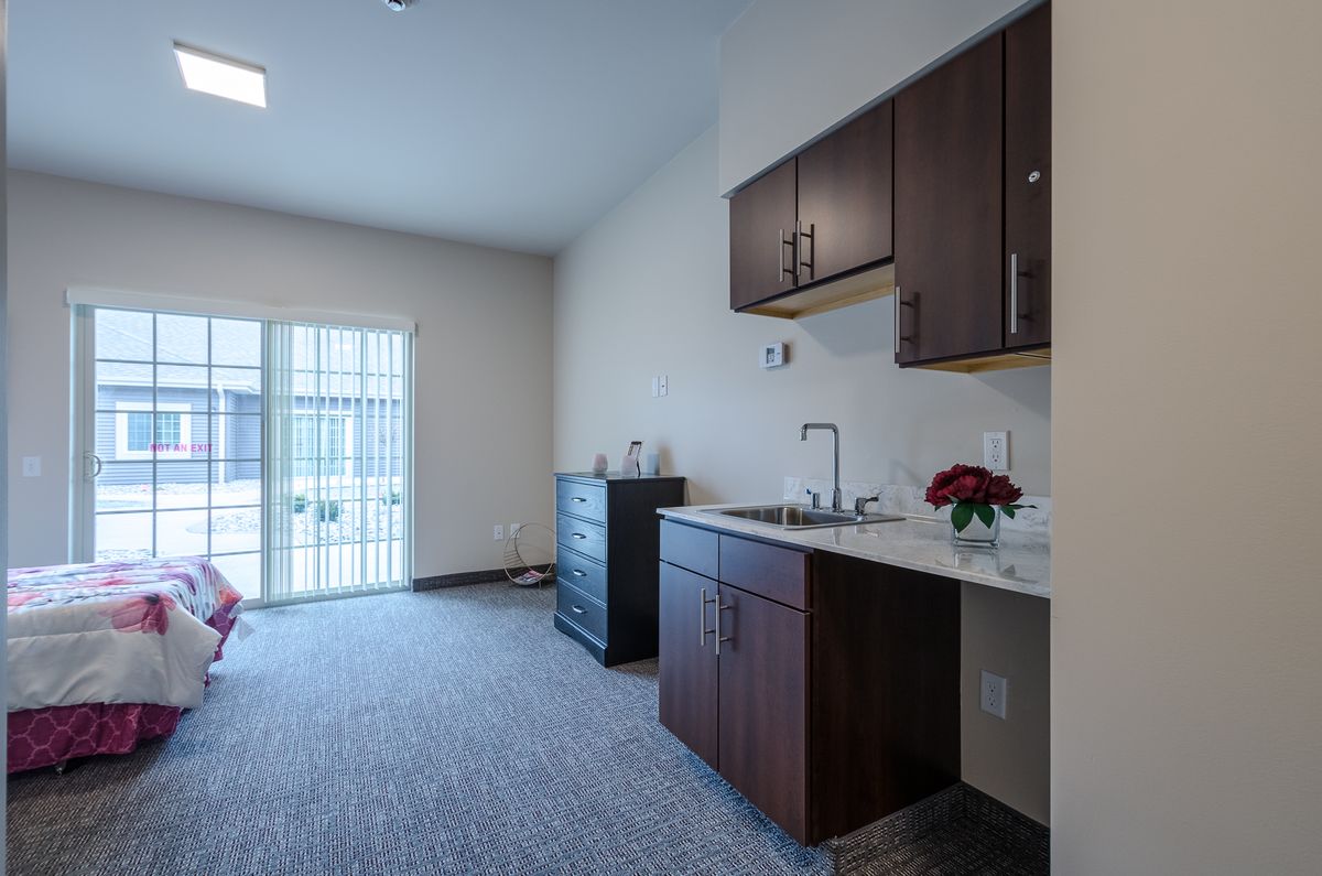 A modern kitchenette with dark wood cabinets, a sink, and bright natural lighting.