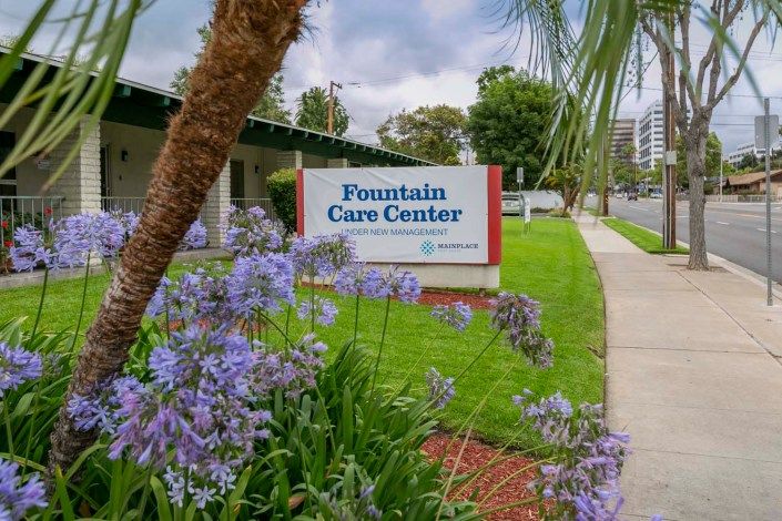 Entrance sign of the Fountain Care Center surrounded by lush greenery and purple flowers.