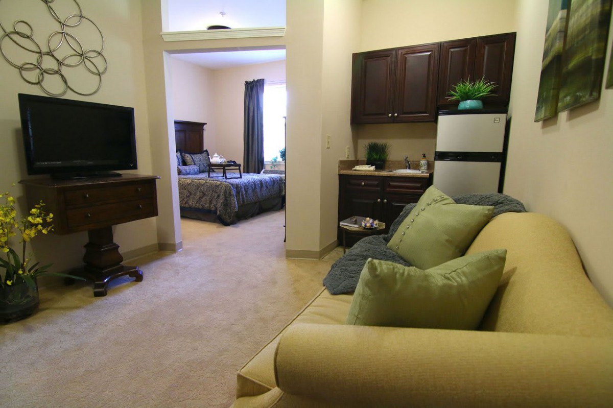 A cozy apartment interior featuring a living area with a sofa and TV, leading to a bedroom.