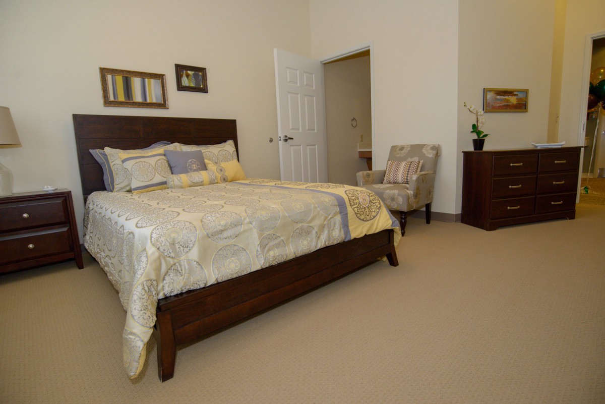 A cozy bedroom with a neatly made bed, an armchair, and a small dresser.