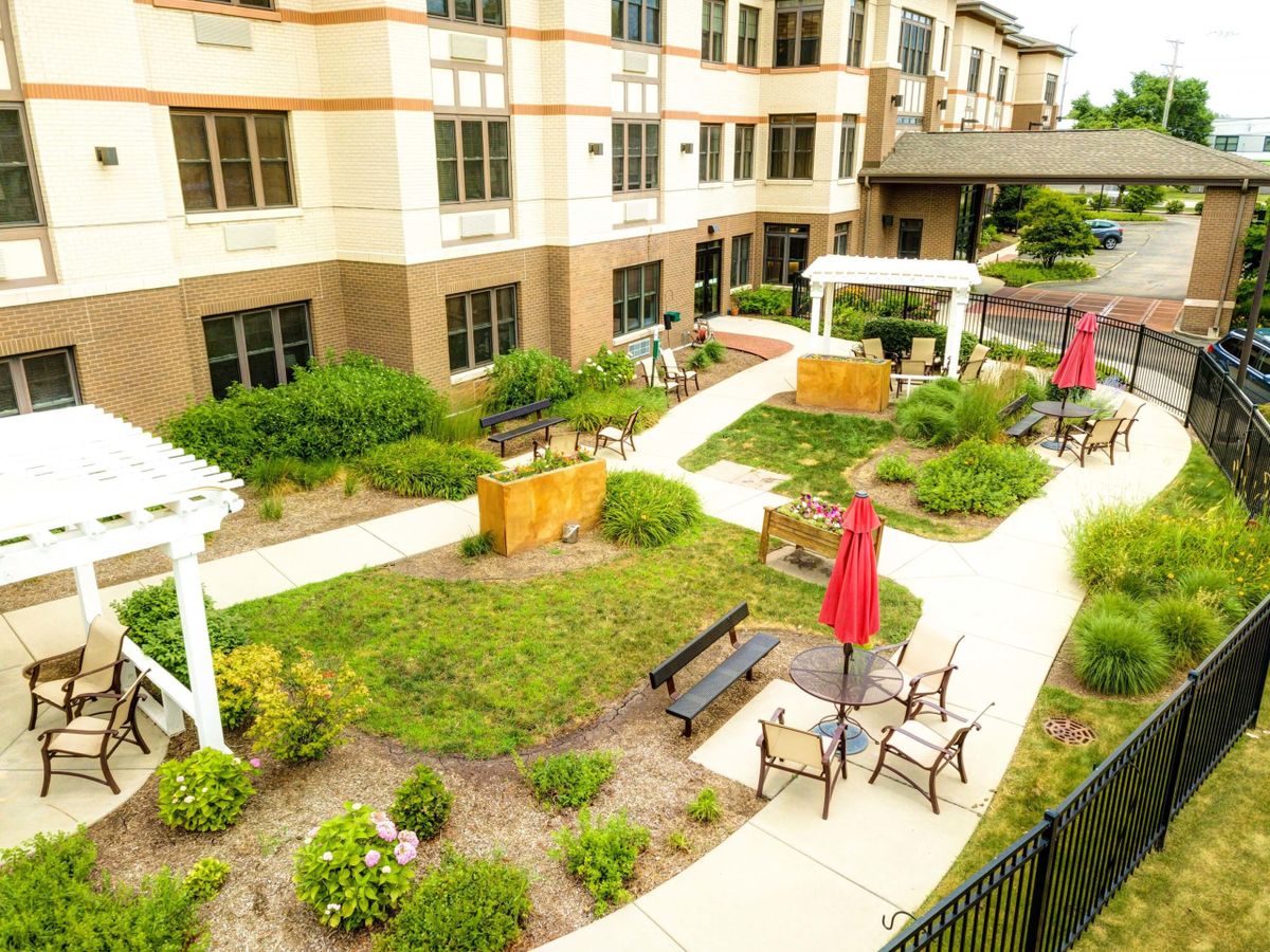 A well-maintained garden area with benches and umbrellas near a residential building.