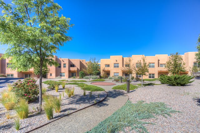 A modern apartment complex with landscaped pathways and desert-style architecture under a clear blue sky.