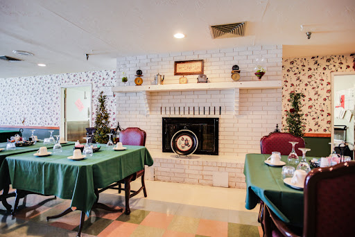 A cozy dining room featuring a white brick fireplace and tables set with green tablecloths.