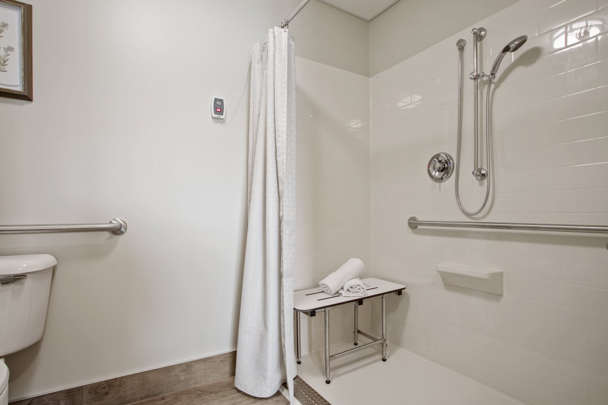 An accessible bathroom with a shower area featuring grab bars, a shower bench, and a white curtain.