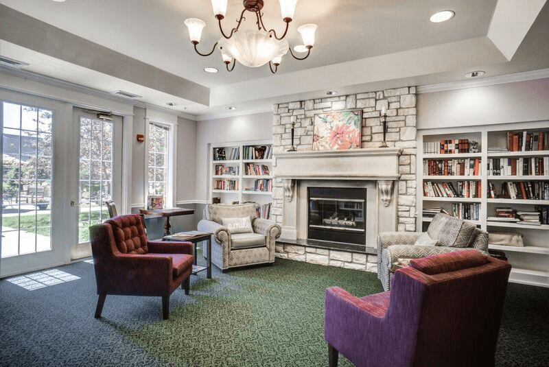 A cozy living room with a fireplace, surrounded by bookshelves and comfortable armchairs.
