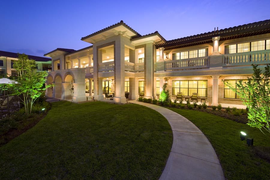 A beautifully lit luxury mansion in the evening with well-manicured landscaping.