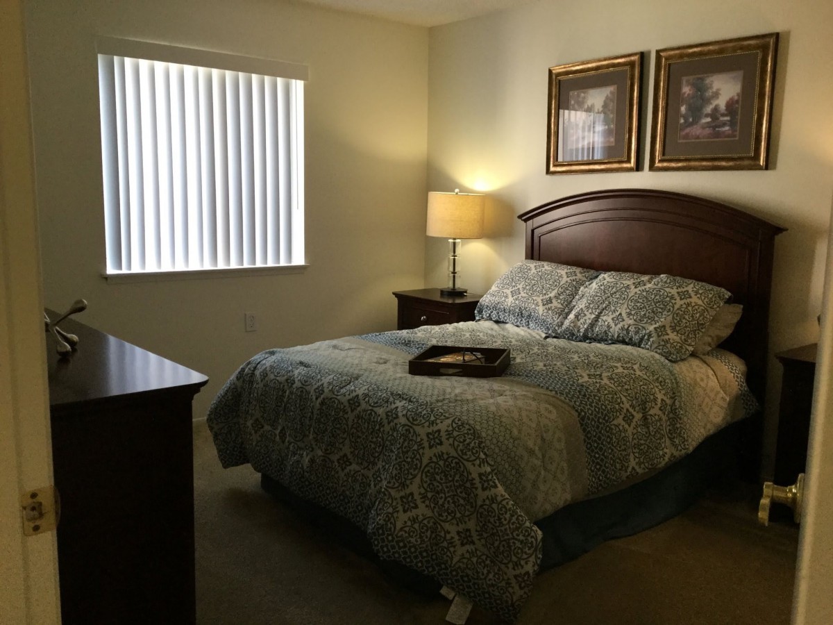 A cozy bedroom with a neatly made bed, bedside lamp, and framed artwork on the wall.