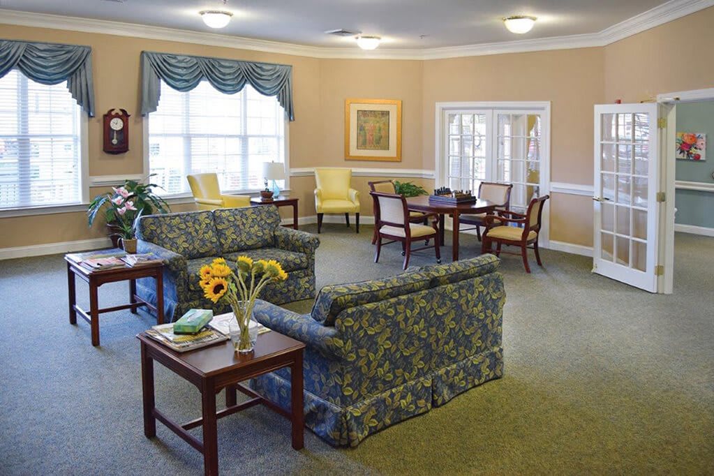 A cozy living room with floral sofas, coffee tables, and bright windows.