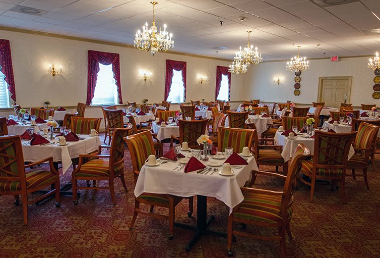 An elegant restaurant dining room with neatly arranged tables and chairs, adorned with chandeliers and red curtains.