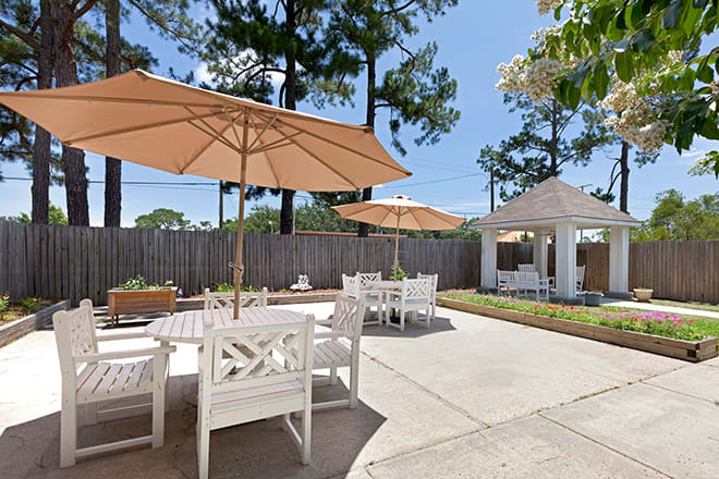 A sunny patio area with tables, chairs, and umbrellas next to a gazebo.