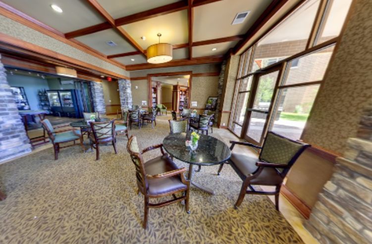 A cozy lounge area with chairs and tables, large windows, and warm lighting.