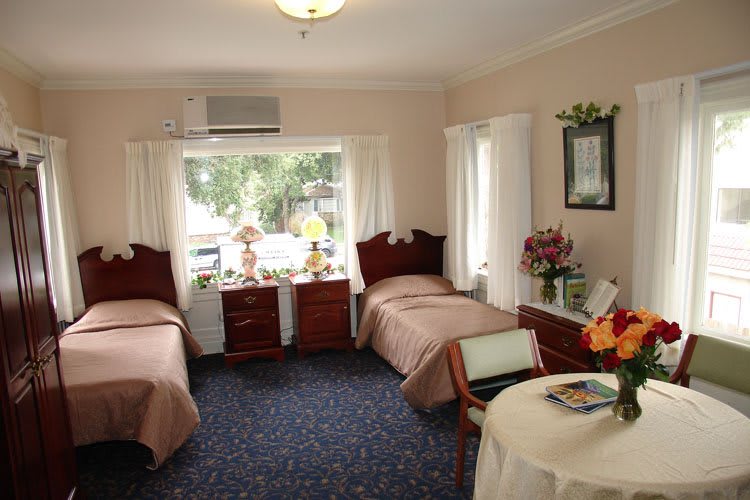 A cozy bedroom with two twin beds, featuring elegant decor and a large window with curtains.
