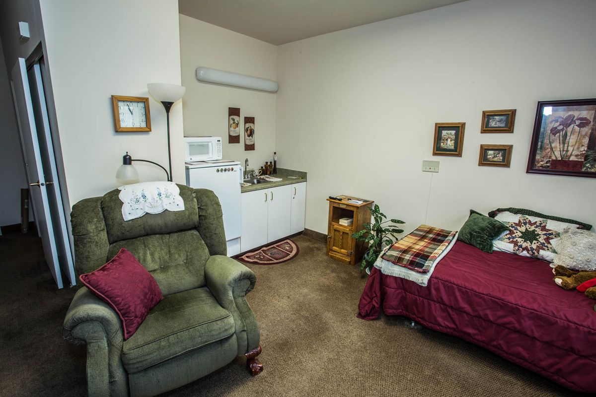 A cozy and compact living space featuring a bed, armchair, and small kitchenette.