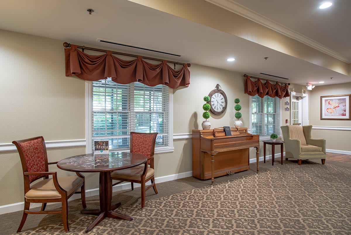 A cozy room with a piano and seating area, featuring elegant decor and large windows.