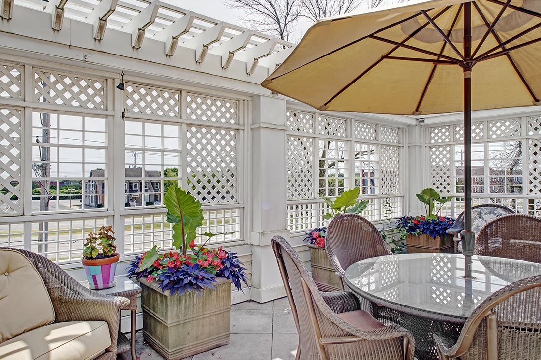 A cozy outdoor patio with a pergola, featuring a table and chairs, potted plants, and a large umbrella.