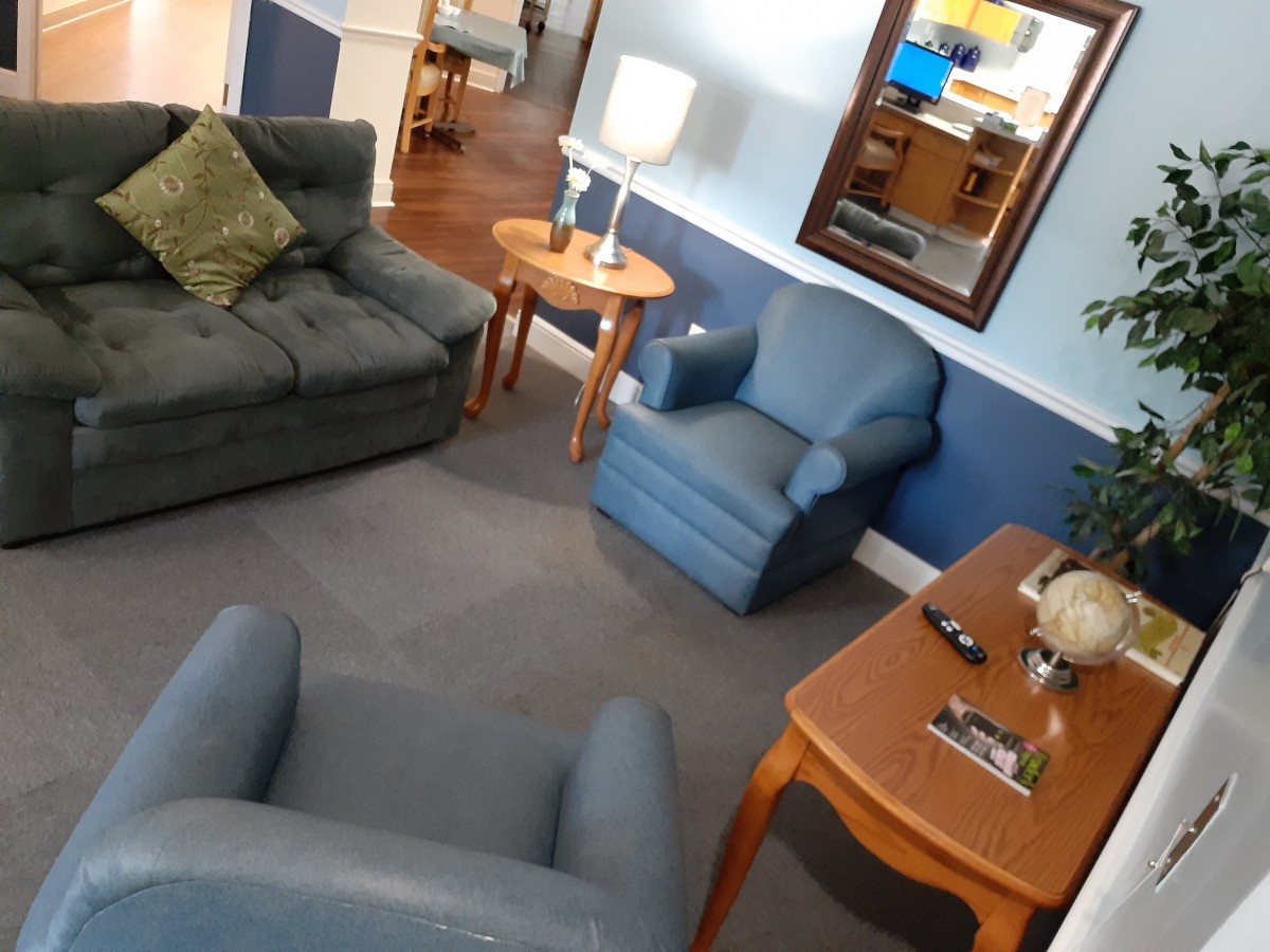 A cozy living room with blue and gray furniture, including sofas, chairs, and a wooden table with a lamp, complemented by a large mirror on the wall.