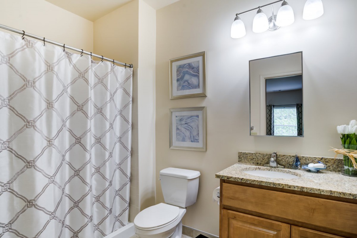 A well-lit bathroom with a shower curtain, toilet, and vanity.