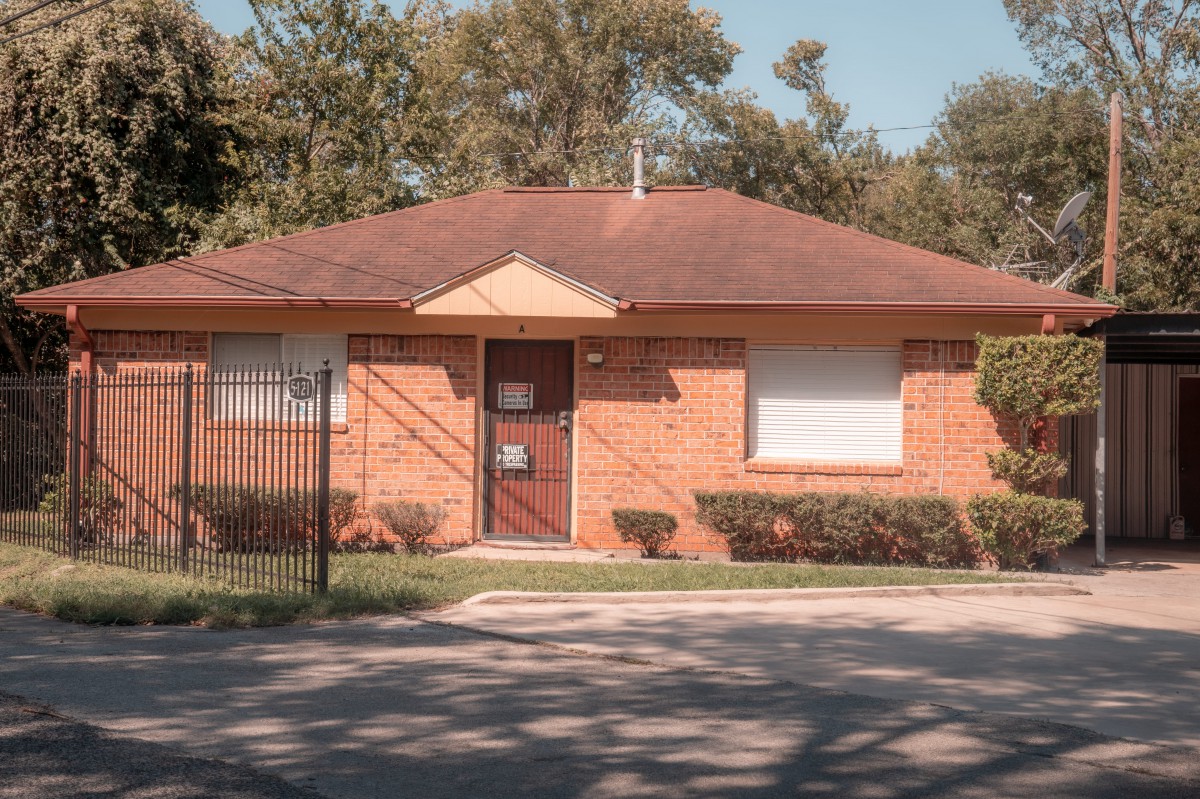 A single-story brick house with a red roof and a small front yard.