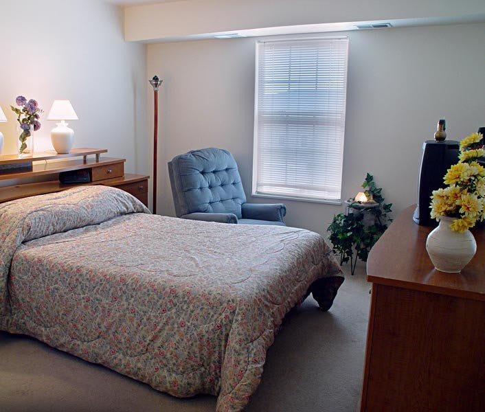 A cozy bedroom with a single bed, chair, and natural light from a window.